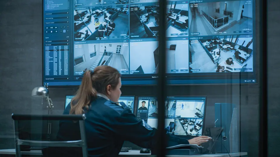 Female CCTV operator works on computer and tablet in monitoring center with security cameras, talks on walkie talkie