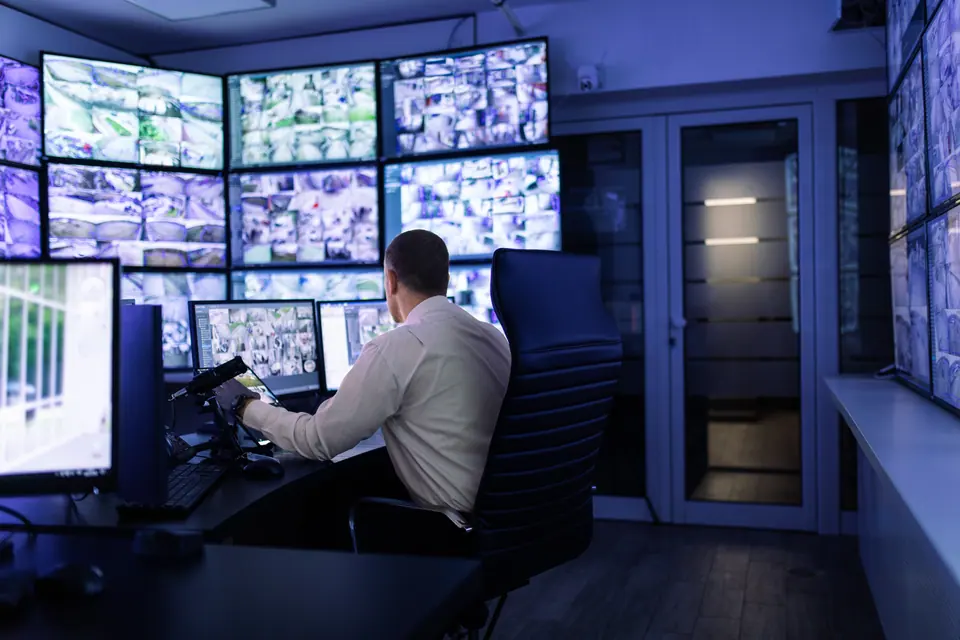 Mature adult man working in surveillance, security and guarding agency and looking at many monitors in front of him