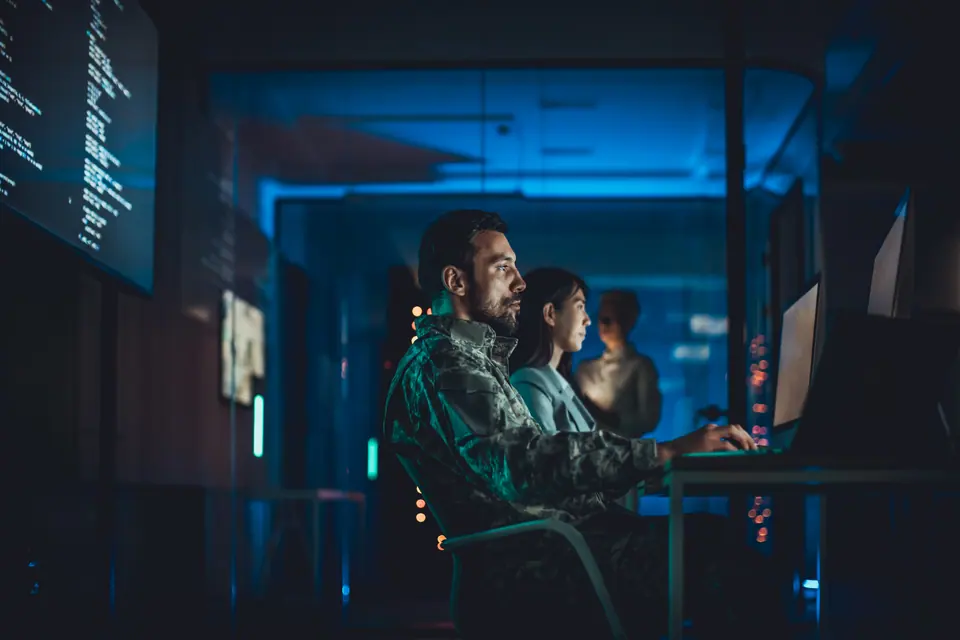 Military technology specialist working at computer in dark control room environment