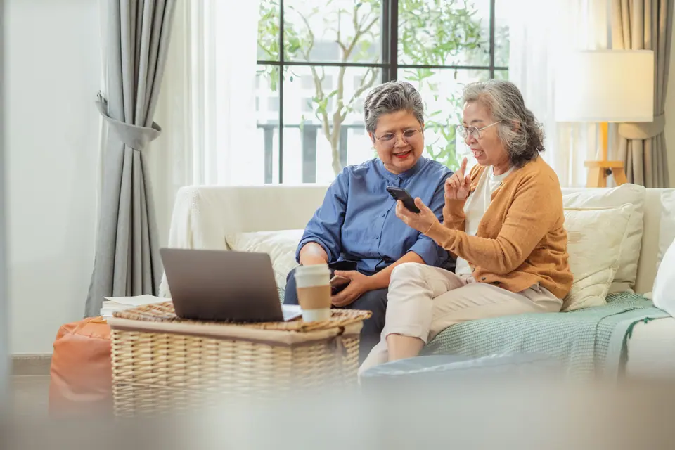 Old Asian retired woman and friends uses AI financial assistant at home to plan pension, insurance, and savings strategy, learning smart chatbot…