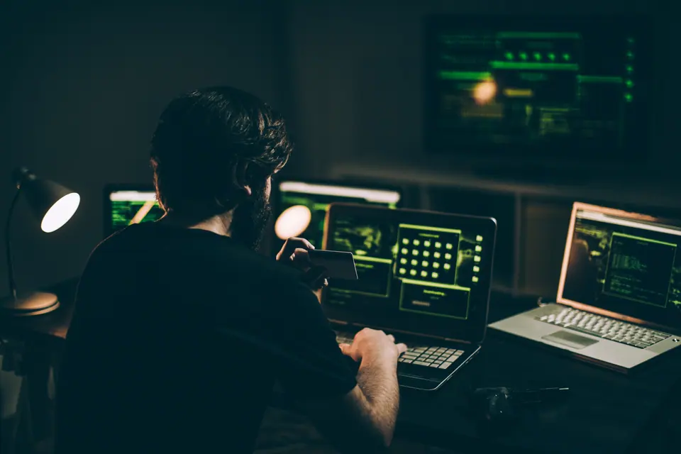 One man, sitting indoors surrounded by computers, hacking crime is in motion, holding a credit card