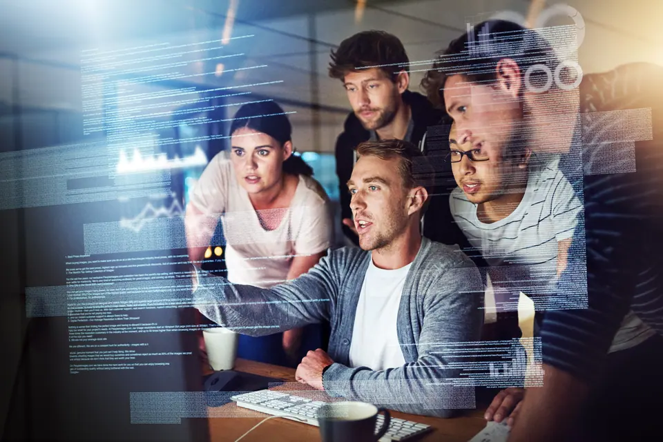 Shot of a group of young people using a computer with a virtual screen during a late night at work