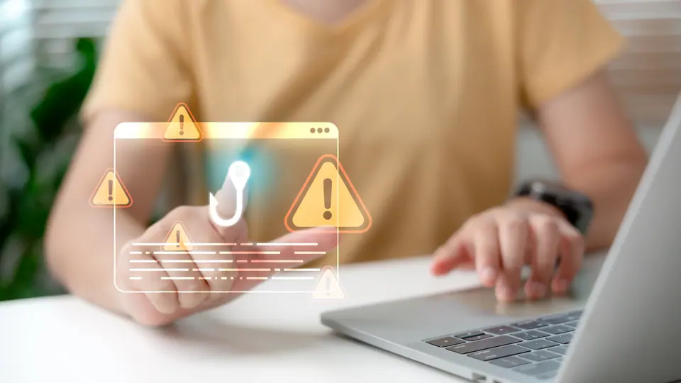 Web phishing and cyber attack warning concept with man using laptop, digital alert icon and exclamation sign representing online scam, fraud detection,…