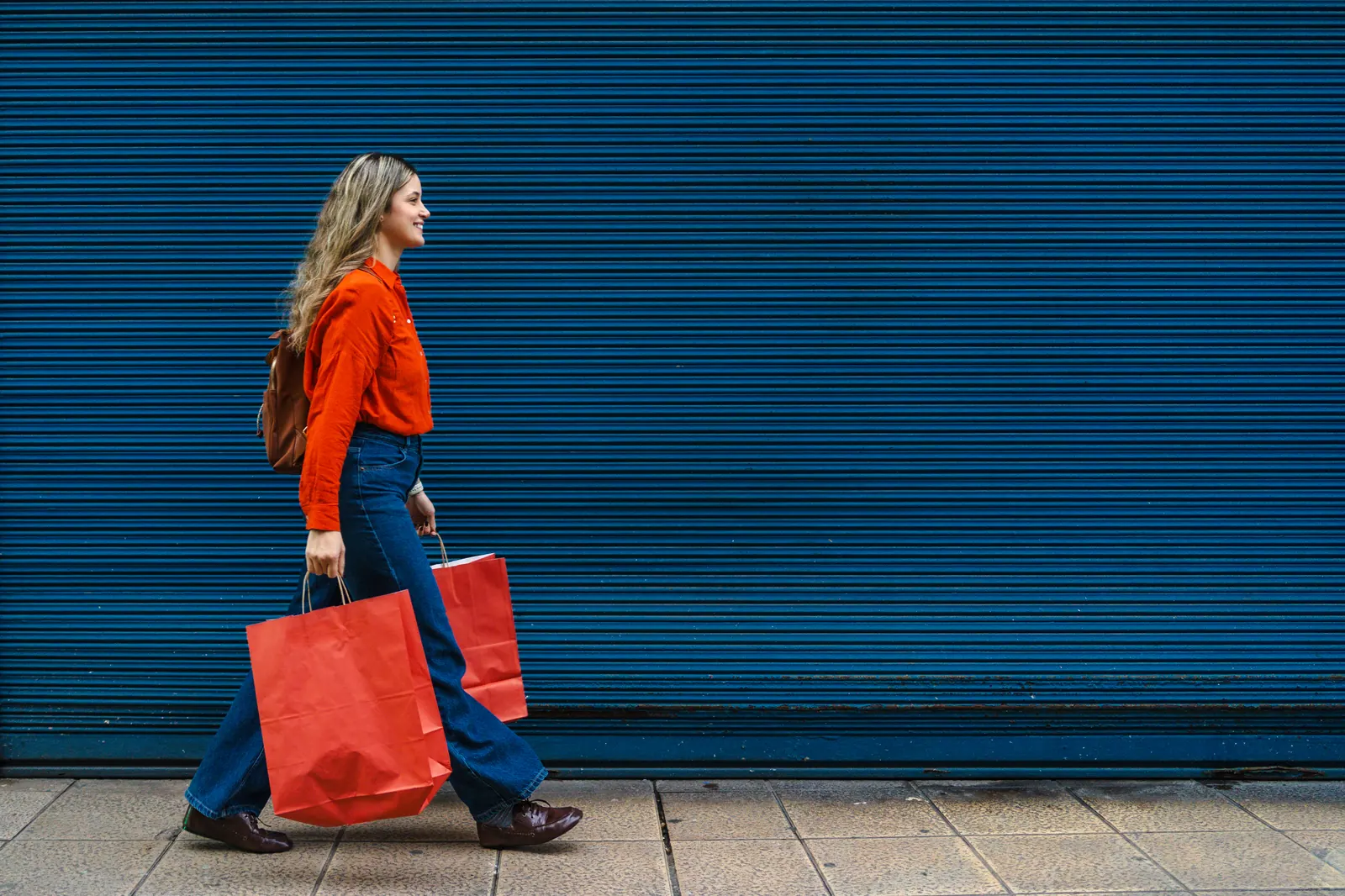 Woman carrying shopping bags past a blue storefront